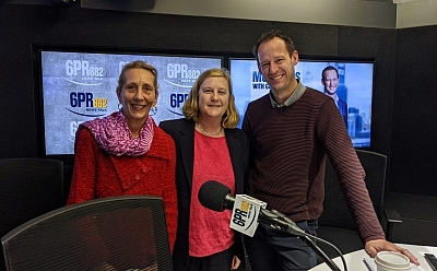 Two women and a man standing in front of 6PR microphone with two television screens behind them
