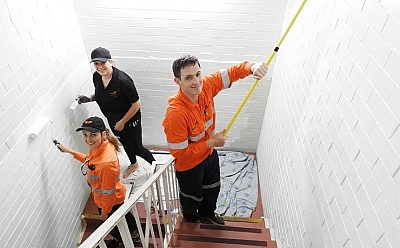 People in a stairwell wearing hi-vis shirts and painting the brick walls white.