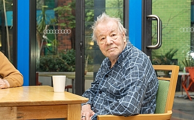 Elderly man sitting at a table looking at the camera.