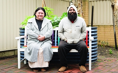 Two people sitting on a colourful outdoor bench in a garden courtyard.