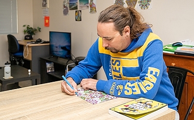 Person in a football jumper sits at a table doing a colouring-in book.